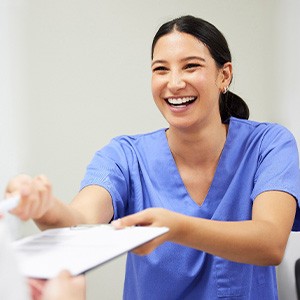 Medical professional in blue scrubs handing paperwork to patient