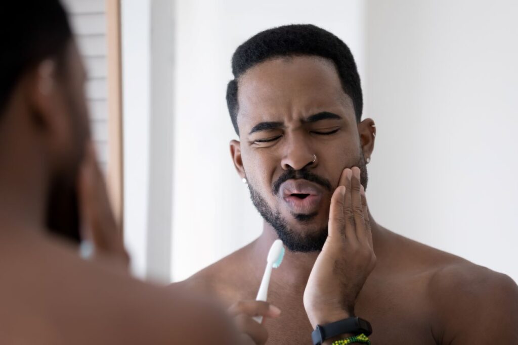 A man experiencing tooth sensitivity while brushing his teeth.